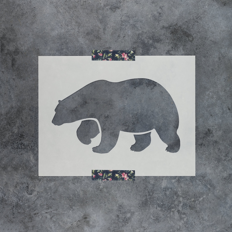 May include: A white stencil of a black bear walking to the right. The stencil is on a grey background.