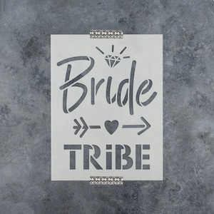 May include: White stencil with the text "Bride Tribe" in a bold, blocky font. Above the text is a stylized diamond with rays of light and an arrow with a heart in the middle.