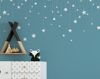 May include: A blue wall featuring white star decals hanging from dotted lines, a triangular wooden shelf containing a small tent-shaped ornament, and a black and white fox figurine atop a white dresser with black polka dots and circular knobs.
