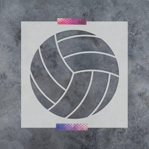 May include: A square stencil featuring a centered volleyball graphic with distinct curved panels. The design is cut out from a light-colored material, revealing the dark textured surface beneath. Two strips of patterned tape secure the top and bottom.