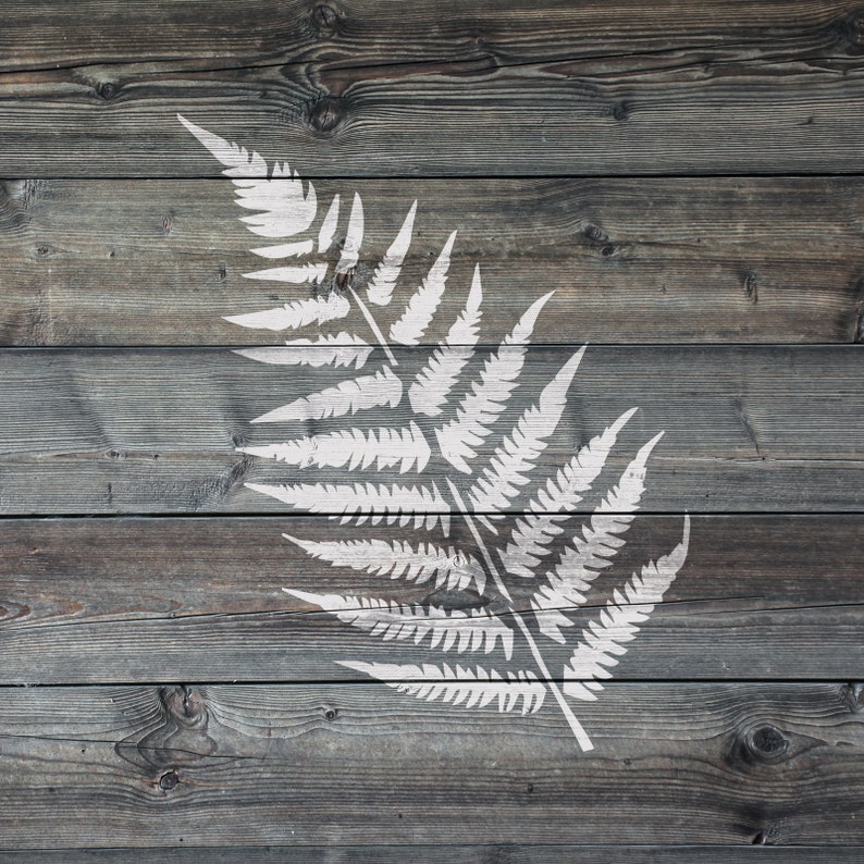 May include: A white fern frond stencil on a weathered grey wood background.