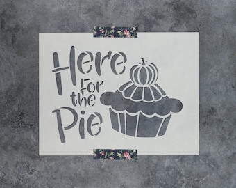 May include: A rectangular stencil featuring the dark gray text Here for the Pie in a stylized font, accompanied by a graphic of a pie topped with a small pumpkin. The stencil is secured at the top and bottom with floral patterned adhesive tape.