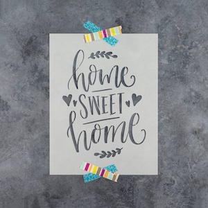 May include: A white stencil with the text "home sweet home" in black script font. The stencil is decorated with small hearts and leafy sprigs.