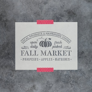 May include: A white stencil with the text "LOCAL PRODUCE & HANDMADE GOODS" in a curved arch above the text "FALL MARKET". The text "open daily" and "fresh picked" are on either side of a pumpkin graphic. Below the text "FALL MARKET" is the text "•PUMPKINS•APPLES•HAYRIDES•".