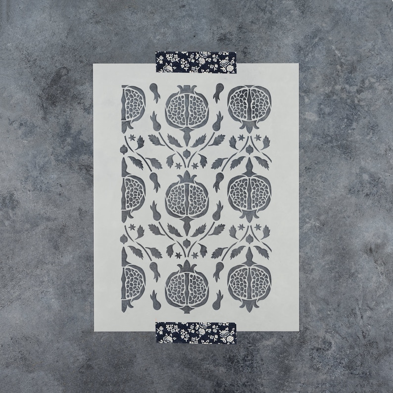 May include: A white stencil with a repeating pattern of pomegranates and leaves. The stencil is made of a thin, flexible material and is designed for use with paint or other mediums.