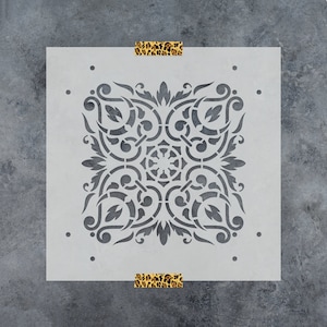 May include: A white stencil with a detailed, intricate, symmetrical design. The design is a repeating pattern of swirls and leaves.
