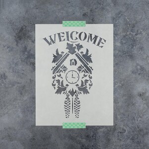 May include: A rectangular stencil featuring a dark gray cutout design of a cuckoo clock with the word WELCOME arched above it. The clock design includes intricate leaf details, a circular clock face, and two hanging pinecone-shaped weights.