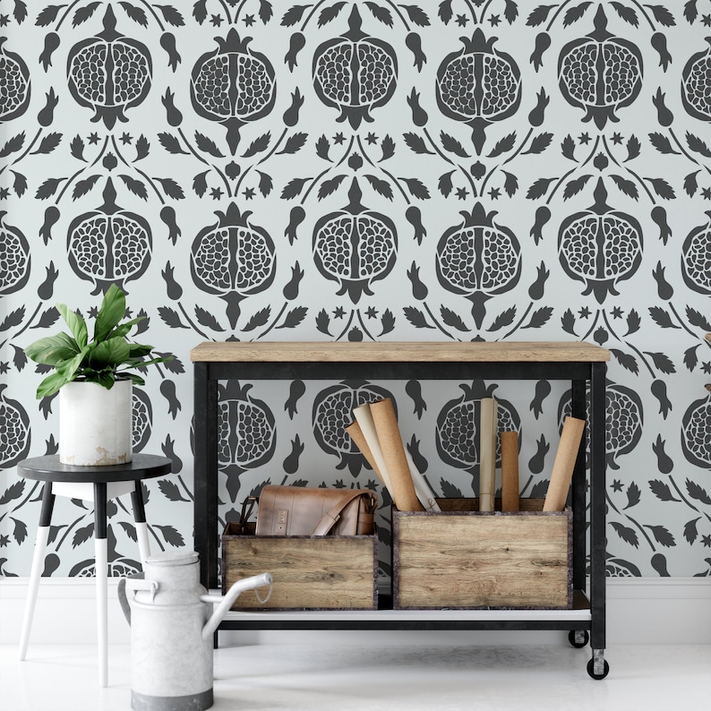 May include: A black metal shelf unit with two wooden shelves. The shelves are filled with rolled up paper and a brown leather bag. The shelf unit is in front of a wall with a white and gray patterned wallpaper featuring a repeating pomegranate design.