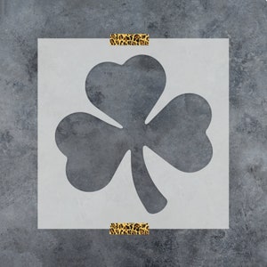 May include: A white stencil of a four-leaf clover, a traditional Irish symbol of good luck. The stencil is taped to a gray textured surface.