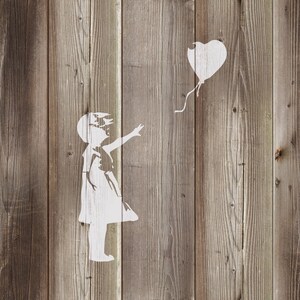 May include: A white stencil of a girl reaching out to a heart-shaped balloon on a wood panel background.