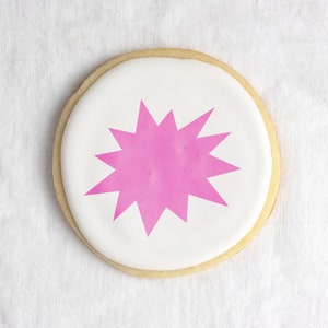 May include: A white sugar cookie with pink icing in the shape of a starburst.