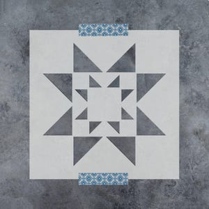 May include: A square stencil featuring a central geometric star pattern composed of dark gray triangles. The stencil has a light gray background and includes two horizontal strips of blue and white floral patterned tape at the top and bottom edges.