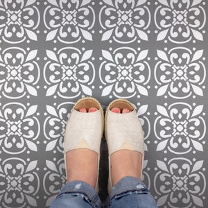 May include: A pair of white canvas shoes with a peep toe design are worn on a gray floor with a white patterned design.