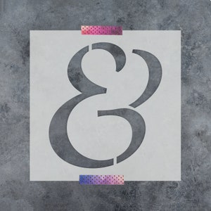 May include: A white stencil with the ampersand symbol cut out. The stencil is taped to a gray textured surface.