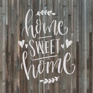 May include: White painted text on a wood background reads "home sweet home" with two small hearts and a leafy design above and below the text.