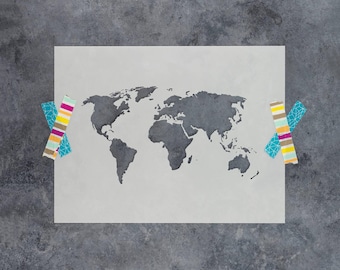 May include: A rectangular stencil featuring a dark gray world map silhouette centered on a light gray background. The stencil is secured at the left and right edges with two pieces of decorative washi tape, each displaying colorful stripes and geometric patterns.