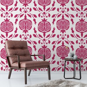 May include: A brown leather armchair with a dark wood frame sits in front of a white wall with a repeating pattern of pink pomegranates. A small black side table with a vase of flowers sits next to the chair.