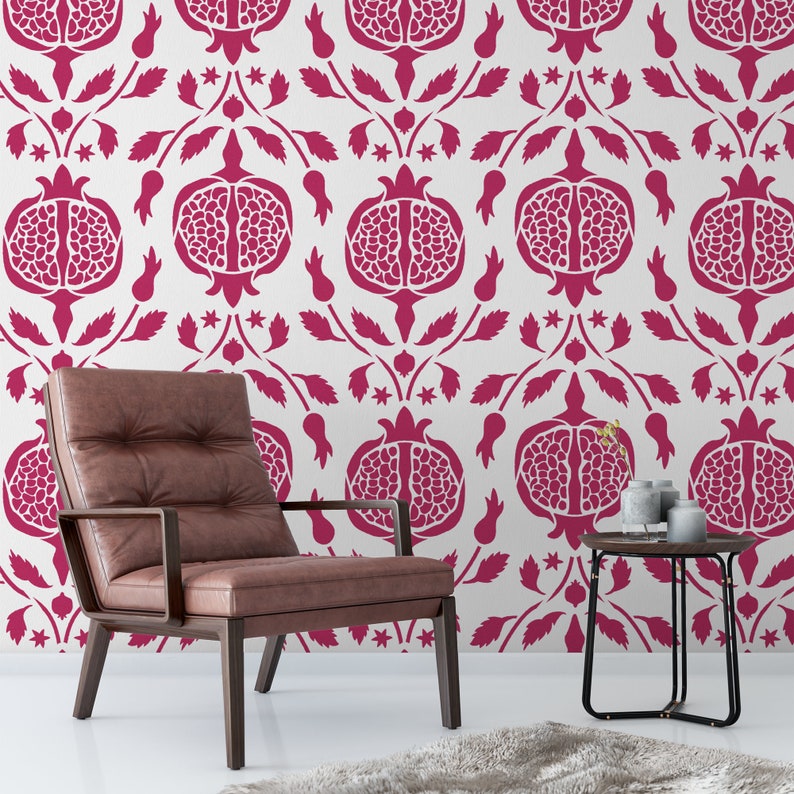 May include: A brown leather armchair with a dark wood frame sits in front of a white wall with a repeating pattern of pink pomegranates. A small black side table with a vase of flowers sits next to the chair.