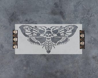 May include: A rectangular stencil featuring a large, detailed moth design with a skull pattern on its thorax. The stencil includes two vertical strips on the left and right sides, each decorated with a series of five small, colorful skull icons.