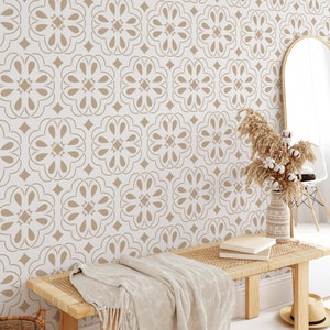 Op de afbeelding: Een witte muur met een beige behang met een herhalend geometrisch patroon. Op de voorgrond staat een houten bank met een gevlochten zitting en een beige deken. Rechts in de afbeelding staat een vaas met gedroogd pampasgras.