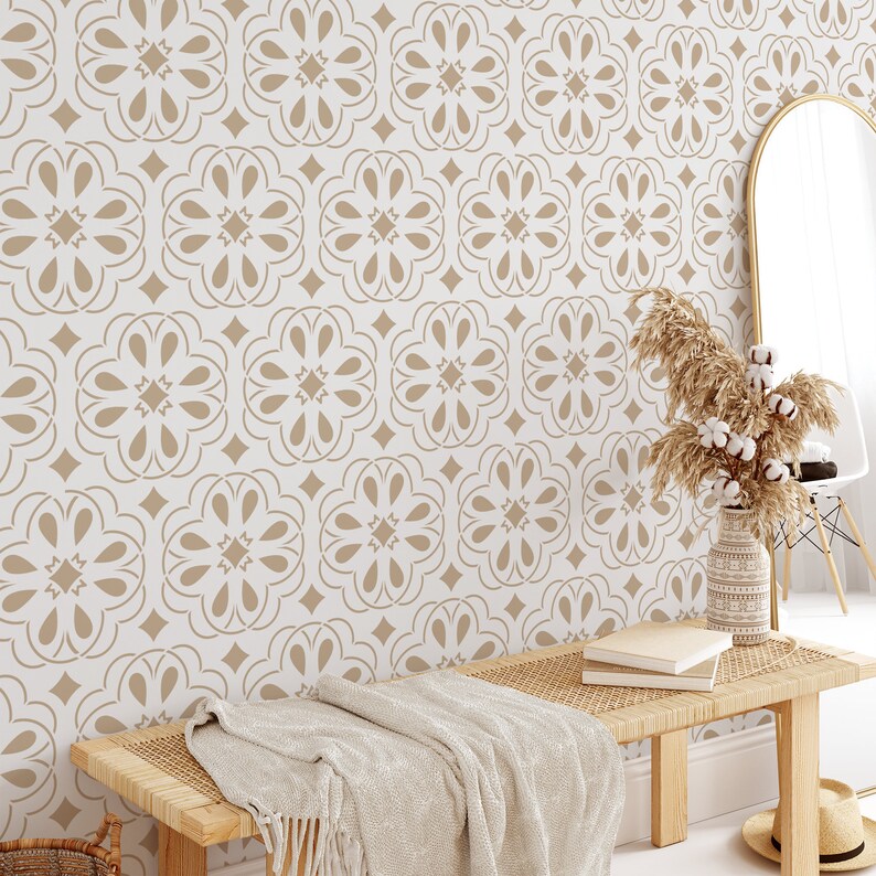 Op de afbeelding: Een witte muur met een beige behang met een herhalend geometrisch patroon. Op de voorgrond staat een houten bank met een gevlochten zitting en een beige deken. Rechts in de afbeelding staat een vaas met gedroogd pampasgras.