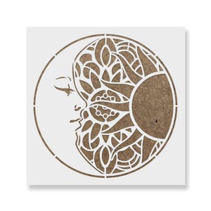 May include: A square stencil featuring a circular design that combines a profile of a human face on the left with an intricate, ornate sun pattern on the right. The design is cut out from a white material, revealing a brown textured surface underneath.