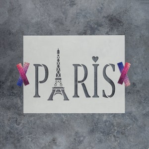 May include: A white stencil with the word "PARIS" and an image of the Eiffel Tower. The stencil is taped to a gray background with pink and blue patterned tape.