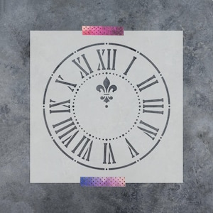 May include: A square stencil featuring a circular clock face design with Roman numerals from I to XII. A fleur-de-lis symbol is centered within the circle, surrounded by a dotted ring. The stencil is held in place by two strips of patterned tape.