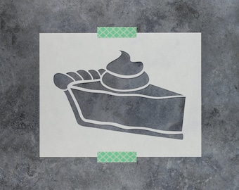 May include: A rectangular stencil featuring a cutout design of a single slice of pie. The pie slice is depicted with a thick, wavy crust edge and a dollop of whipped cream on top. The stencil is held in place by two small pieces of green tape.
