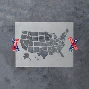 May include: A stencil of the United States of America, showing the outline of each state. The stencil is on a gray background and is surrounded by two red, white, and blue stars.