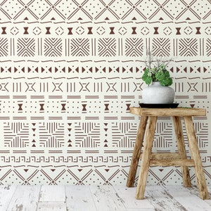 May include: A wooden stool with a white ceramic vase filled with green plants, set against a wall with a brown and white geometric pattern.