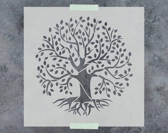 May include: A square, semi-transparent stencil featuring a detailed cutout of a tree with a thick trunk, spreading branches, numerous leaves, and exposed roots. The stencil is secured at the top and bottom edges with small pieces of patterned tape.