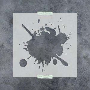 May include: A square, semi-transparent stencil sheet featuring a dark gray ink splatter design with various irregular droplets and splashes. The stencil is secured at the top and bottom edges with small strips of light green patterned adhesive tape.