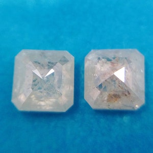 May include: Two clear, square-shaped diamonds on a blue background.