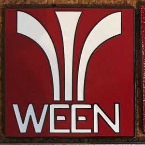 May include: A red square pin with a white stylized design and the word "WEEN" in white letters.