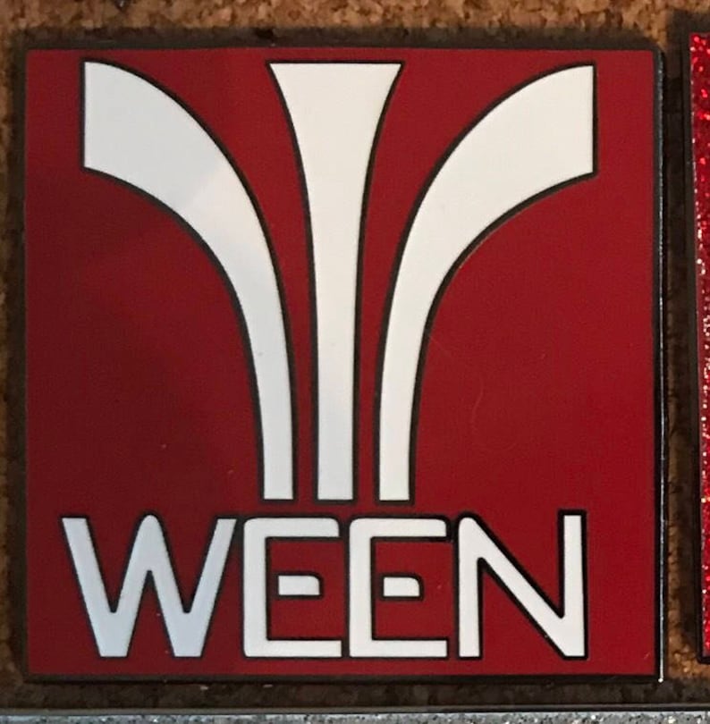 May include: A red square pin with a white stylized design and the word "WEEN" in white letters.