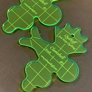 May include: Two green plastic quilting templates, one large and one small, shaped like a clamshell. The templates are labeled "Quiltoff" and "Clamshell #1" with the website address "www.juliaquiltoff.com".