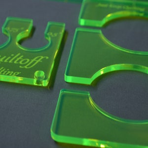 May include: Green plastic quilting templates with different sized circles. The templates are labeled with the measurements 1.75, 2.0, and 4.5. The templates are labeled "Quiltoff Free-Motion Quilting".