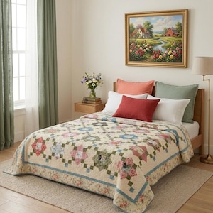 Può includere: Una scena di camera da letto con un letto coperto da una trapunta floreale in crema, rosa, blu e verde. Il letto ha diversi cuscini di diversi colori. Un dipinto di paesaggio incorniciato è appeso sopra il letto. Le tende verdi incorniciano una finestra.