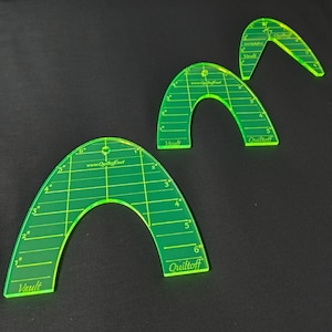 May include: Three green plastic quilting rulers with a grid pattern and measurements in inches. The rulers are shaped like arches and have the text "Quiltoff" and "Vault" printed on them.