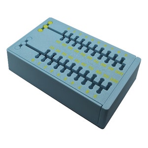 May include: A light blue plastic tool with multiple slots and yellow markings. The tool has a rectangular shape with a series of evenly spaced slots and numbers from 5 to 100. Three yellow dots are visible on the top left.