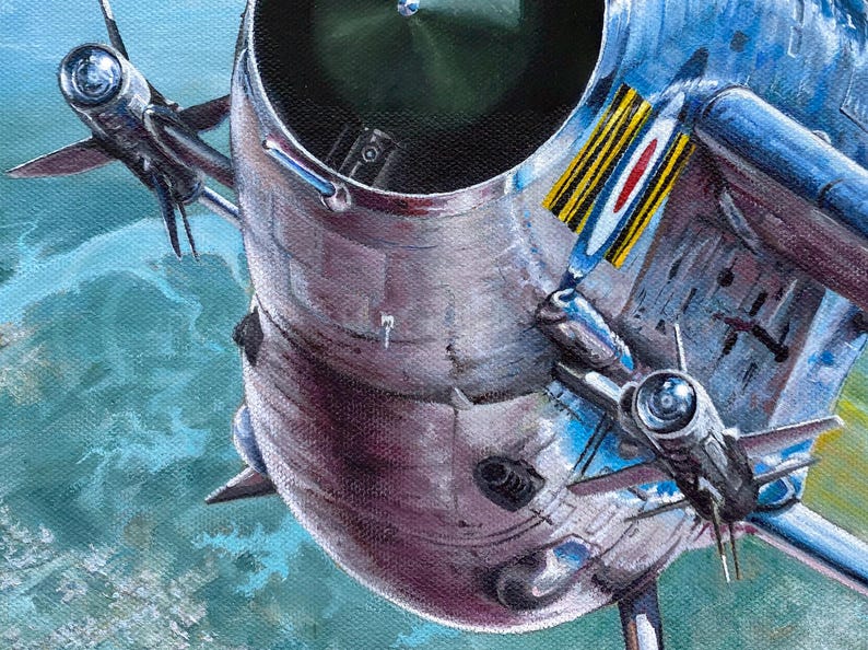 May include: A close-up of a silver and blue fighter jet with a red, white, and blue roundel on the side. The jet is flying over a green and blue landscape.
