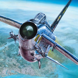 May include: A silver and blue fighter jet flies over a city and water. The jet has a large engine and a long, pointed nose.