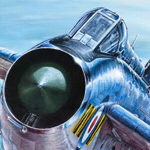 May include: A close-up of a blue and silver fighter jet with a large, round engine intake. The jet has a round canopy and a distinctive roundel on the side.