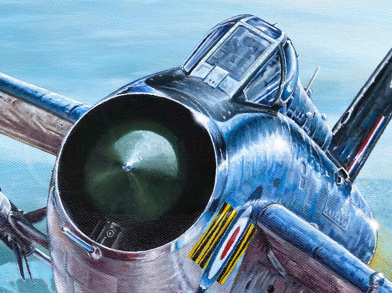 May include: A close-up of a blue and silver fighter jet with a large, round engine intake. The jet has a round canopy and a distinctive roundel on the side.