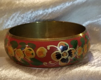 May include: A red brass bangle with a floral design. The flowers are painted in yellow, orange, black, and green.
