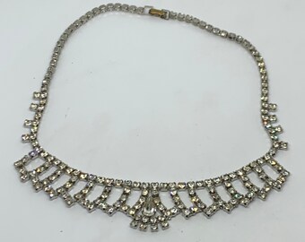 May include: A silver rhinestone necklace with a teardrop-shaped pendant. The necklace has a delicate, geometric design.