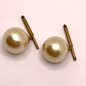 May include: A pair of gold-tone earrings with faux pearl accents. The pearls are round and off-white in colour.