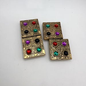 May include: Four gold-toned square vintage earrings with colorful jewel accents. Each earring features four round jewels in red, purple, green, and black, set within a decorative pattern. The earrings are displayed on a white surface.