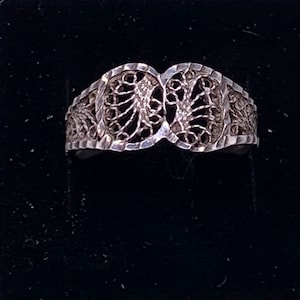 May include: A silver filigree ring with a delicate, intricate design. The ring is made of two overlapping circles with a floral pattern.